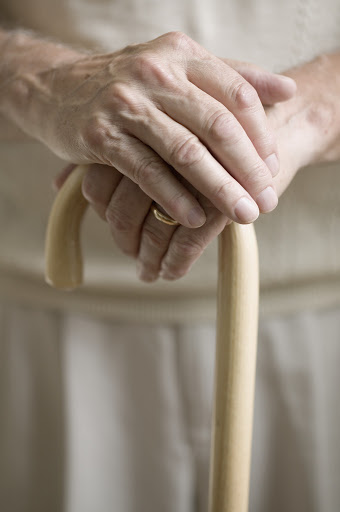 An older adult holding a walking stick with both hands